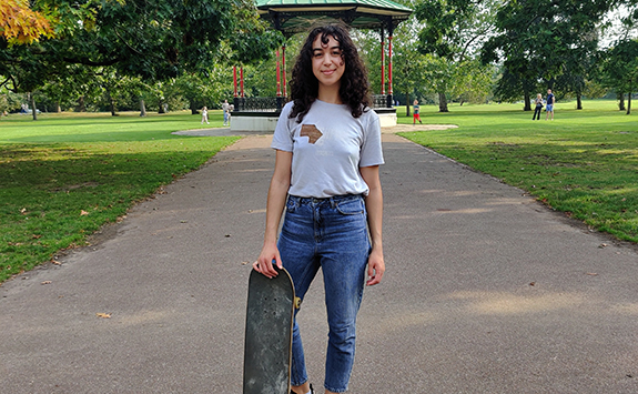 Woman standing in a park on a sunny day holding a skateboard